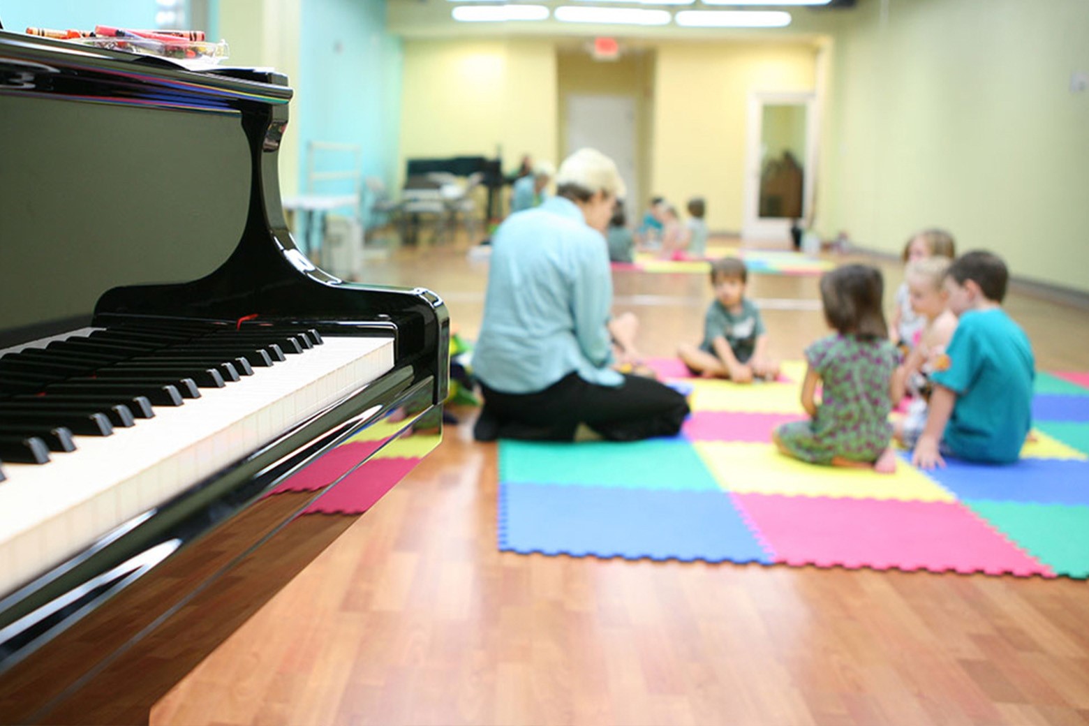 teacher and children playing music in the background, piano in foreground