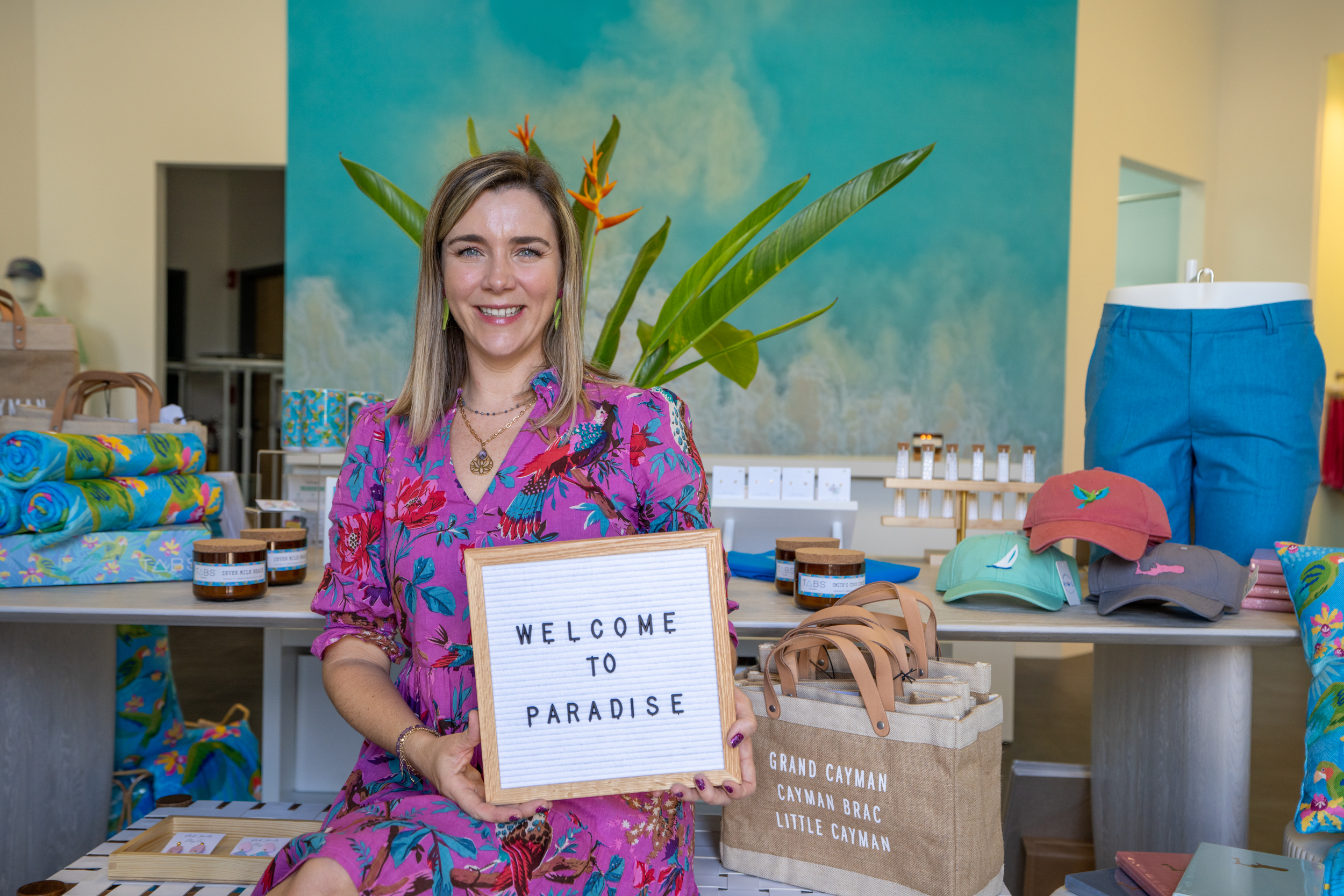 Woman in colour dress holding a "Welcome to paradise" sign