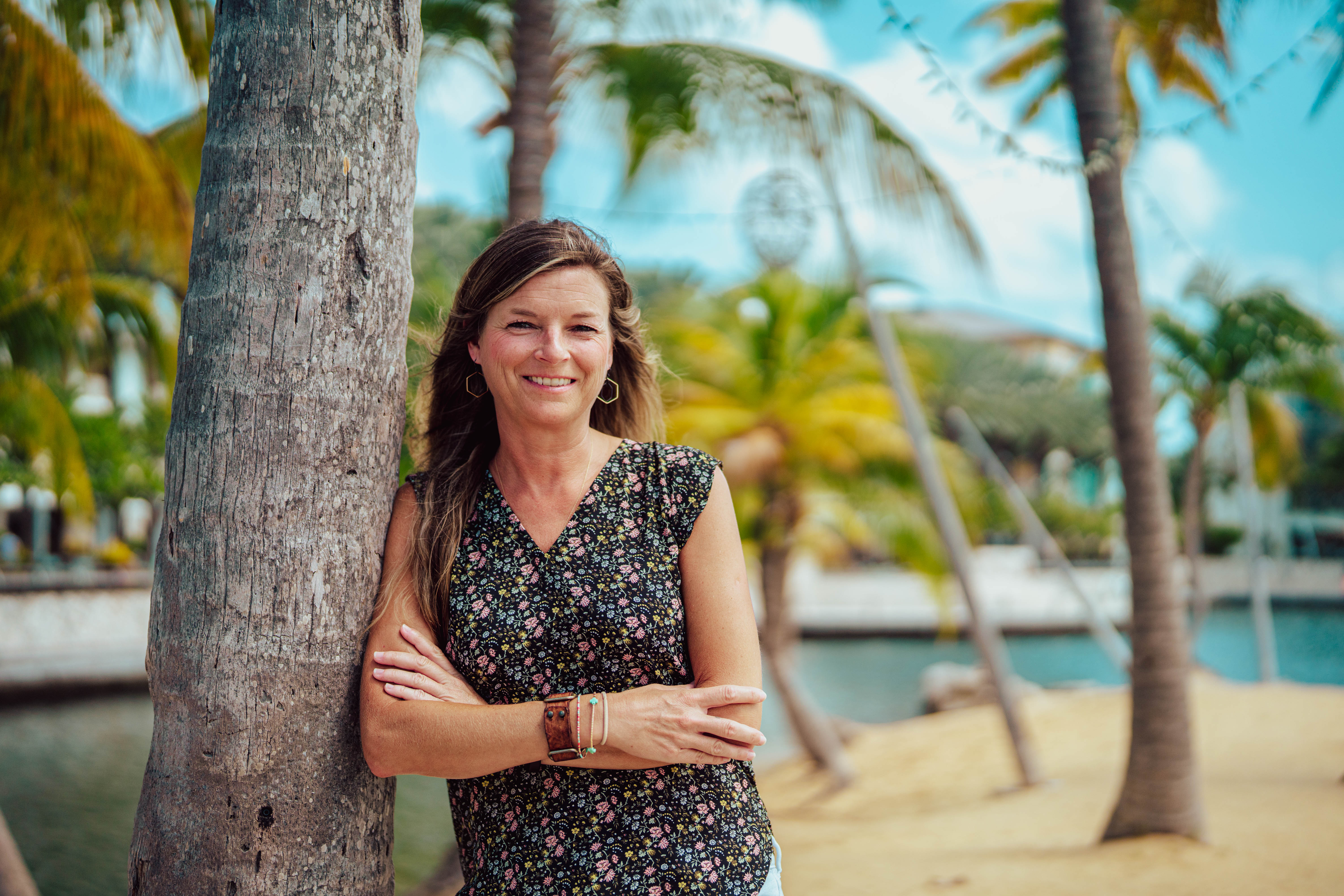 Woman leans on palm tree and smiles at camera